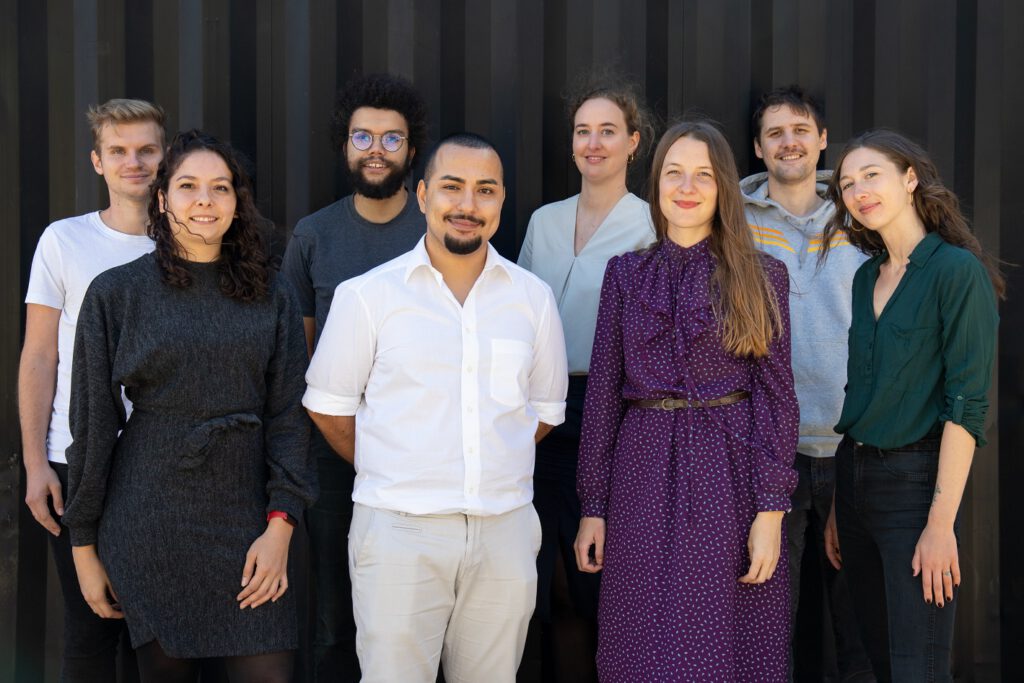 Die Trainees von Durchgang drei stehten für ein Gruppenfoto vor einer schwarzen Container Wand.