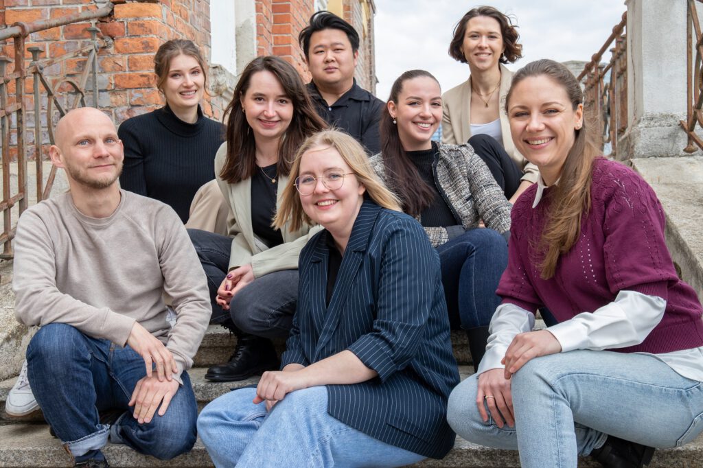 Die Trainees aus Durchgang vier sitzen für ein Gruppenfoto auf Stiegen.